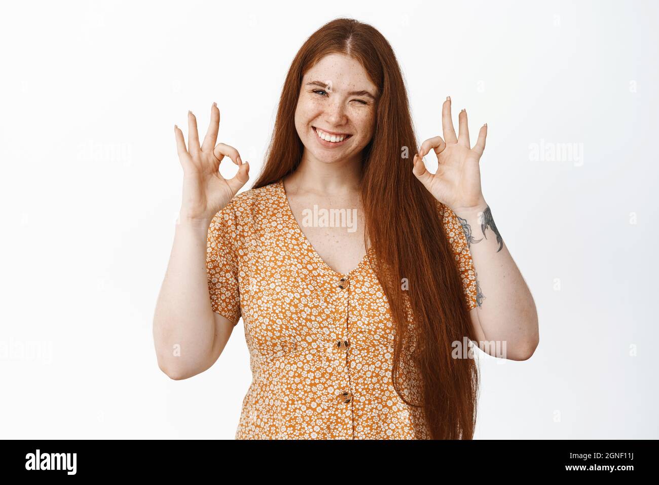 Cute smiling redhead girl showing okay gestures, winking and looking pleased, recommending smth, praise and compliment, white background Stock Photo