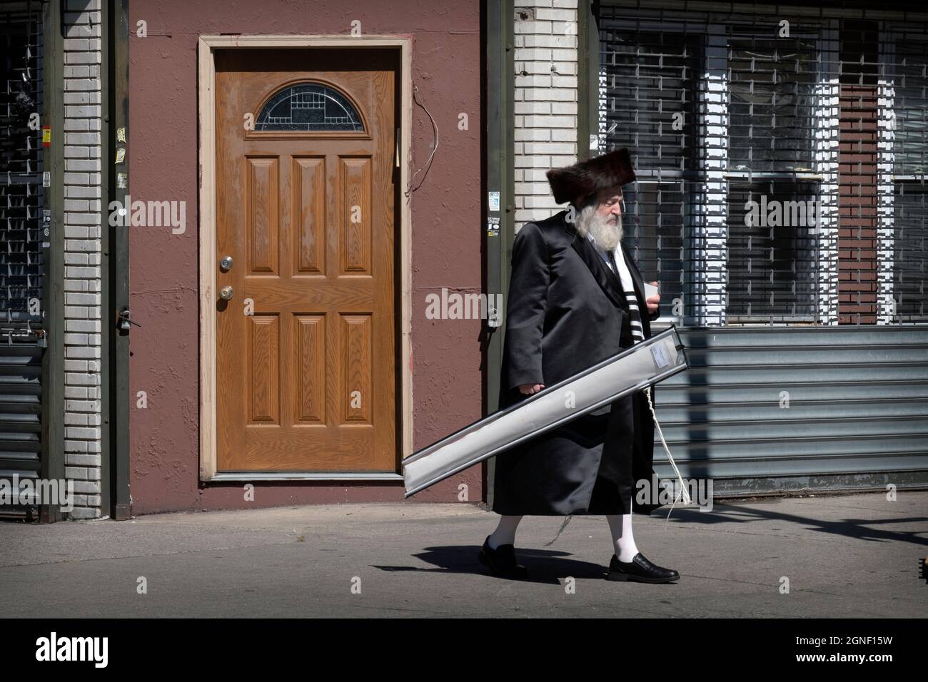 On Sukkos, an orthodox Jewish man walks from synagogue carrying an esrog & lulav and wearing a shtreimel. In Williamsburg, Brooklyn, New York City. Stock Photo
