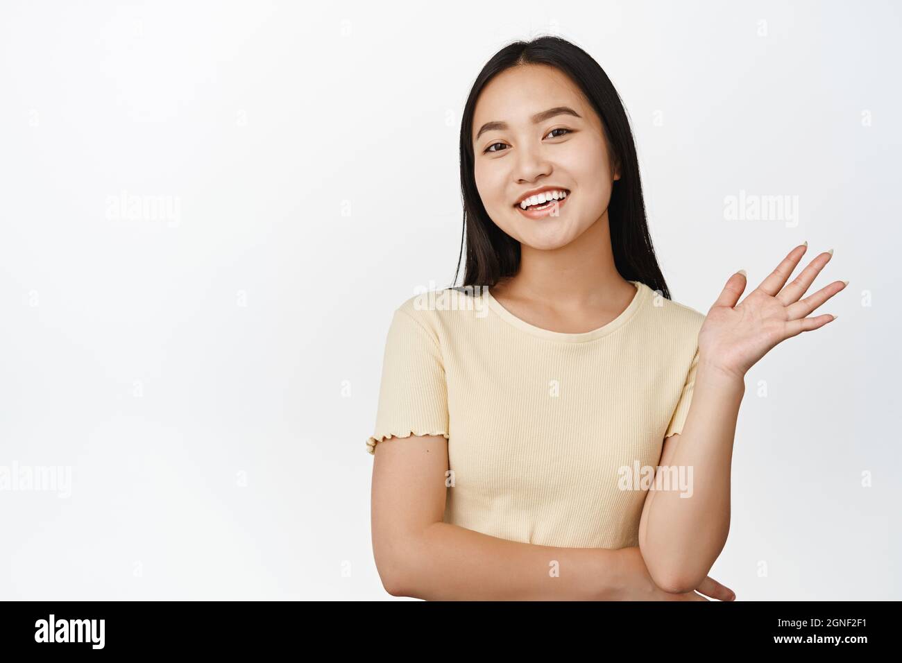 Beautiful young asian girl saying hello, smiling and looking friendly ...