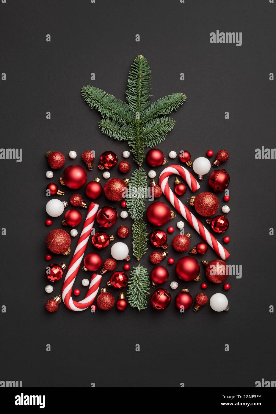 Conceptual Christmas card with holiday gift box made from a candy cane, Christmas balls, and fir tree branches on black background Stock Photo