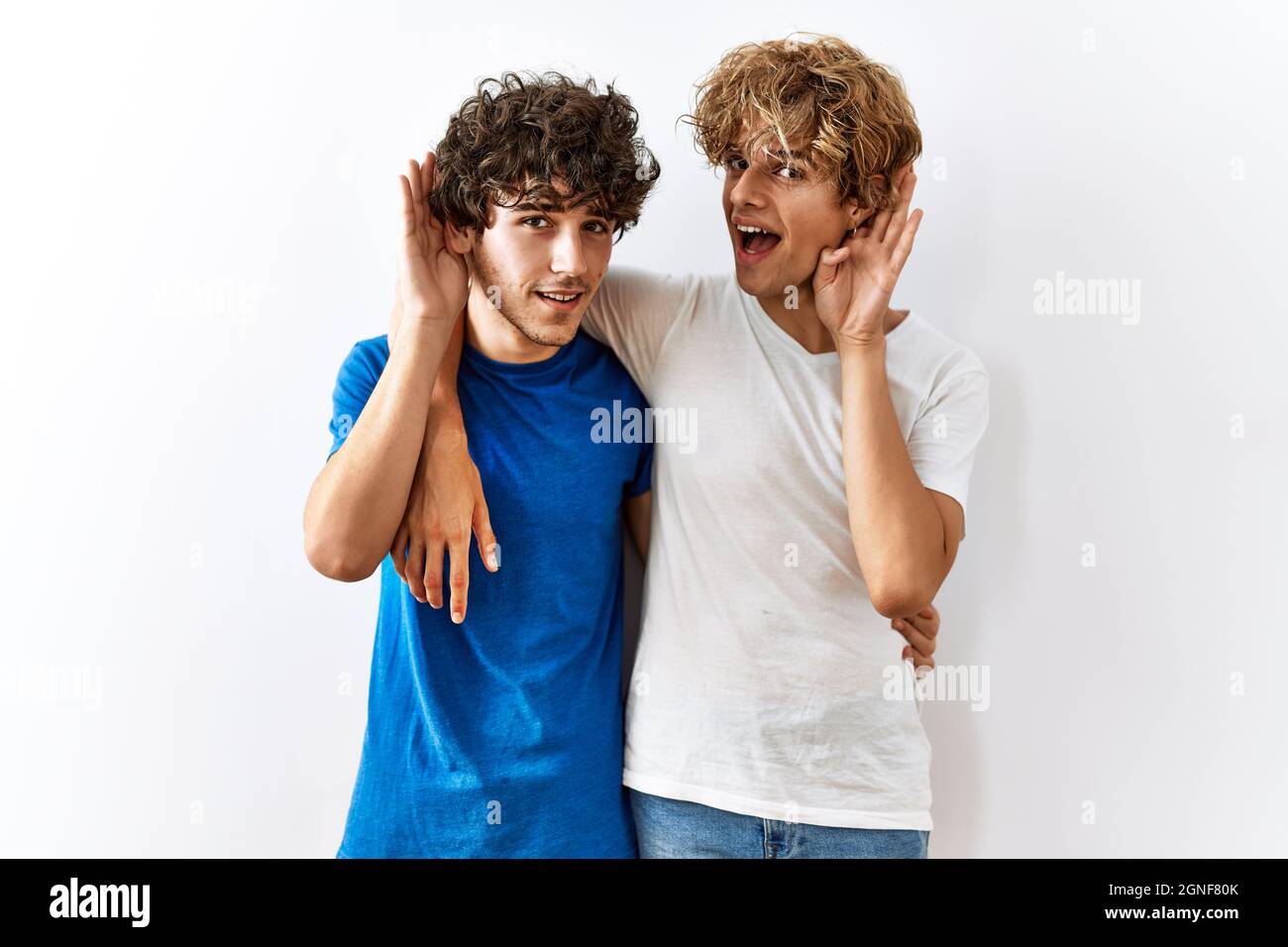 Young gay couple standing together over isolated background smiling with  hand over ear listening an hearing to rumor or gossip. deafness concept  Stock Photo - Alamy