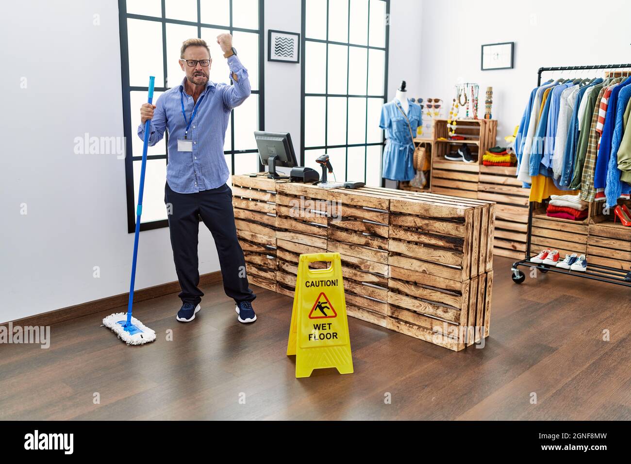 Middle age man working at retail boutique cleaning the floor annoyed and frustrated shouting with anger, yelling crazy with anger and hand raised Stock Photo