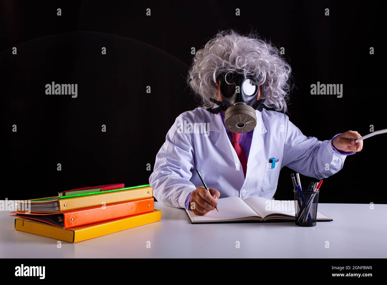 Crazy science teacher in white coat with unkempt hair sitting at the desk  wears a gas mask Stock Photo