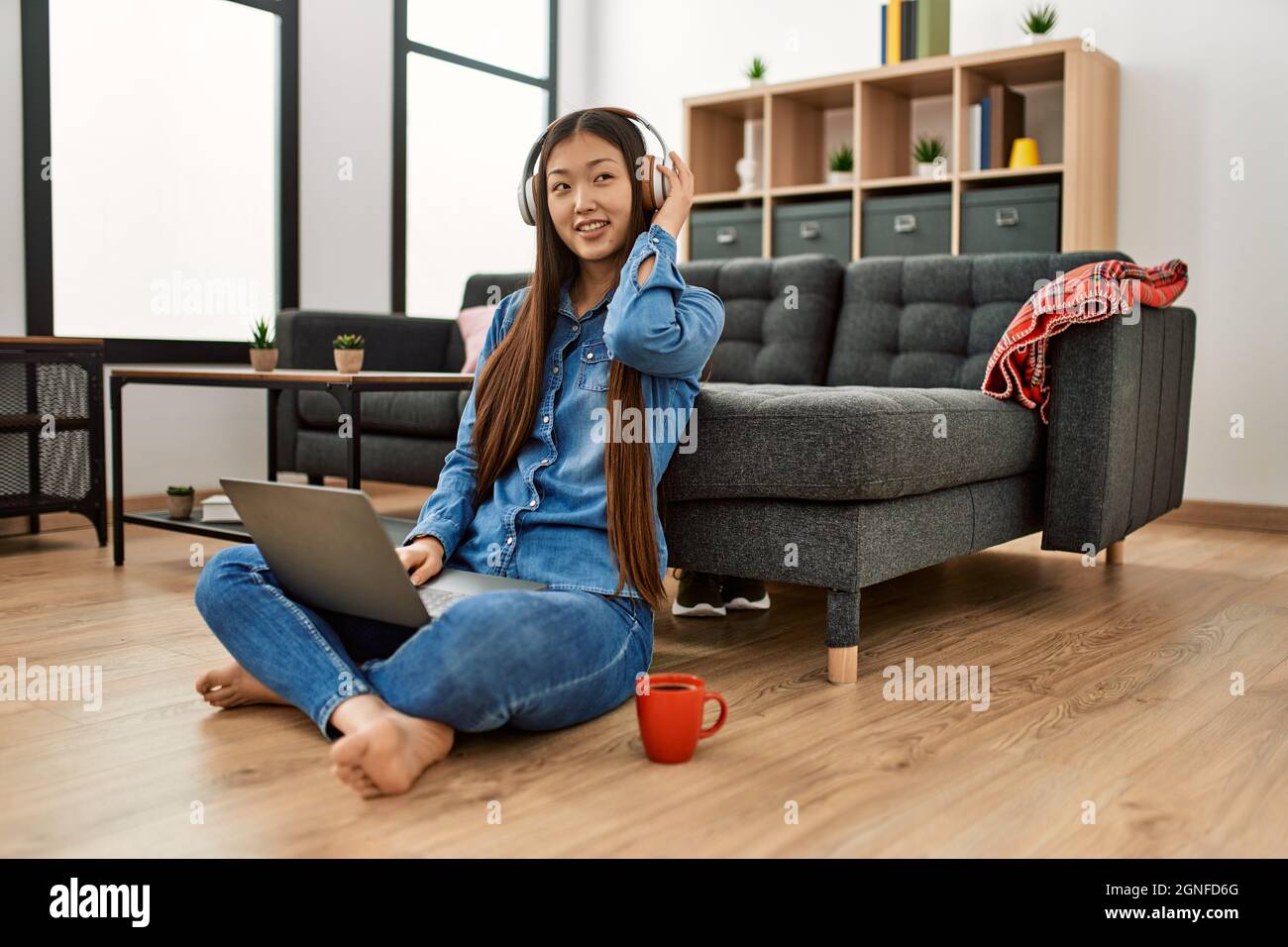 Young chinese girl using laptop and headphones sitting on the floor at ...