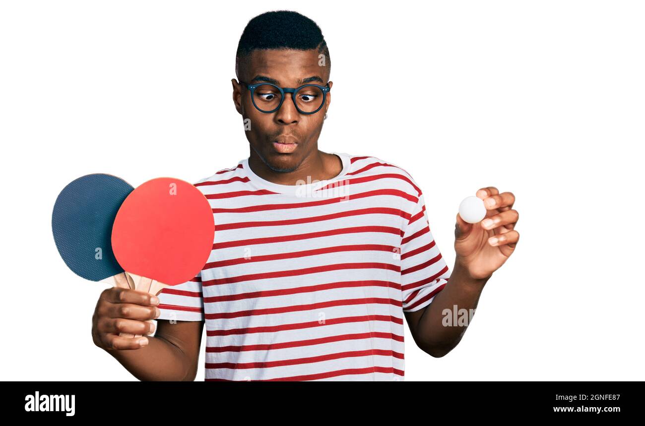 Young african american man holding red ping pong rackets and ball making  fish face with mouth and squinting eyes, crazy and comical Stock Photo -  Alamy