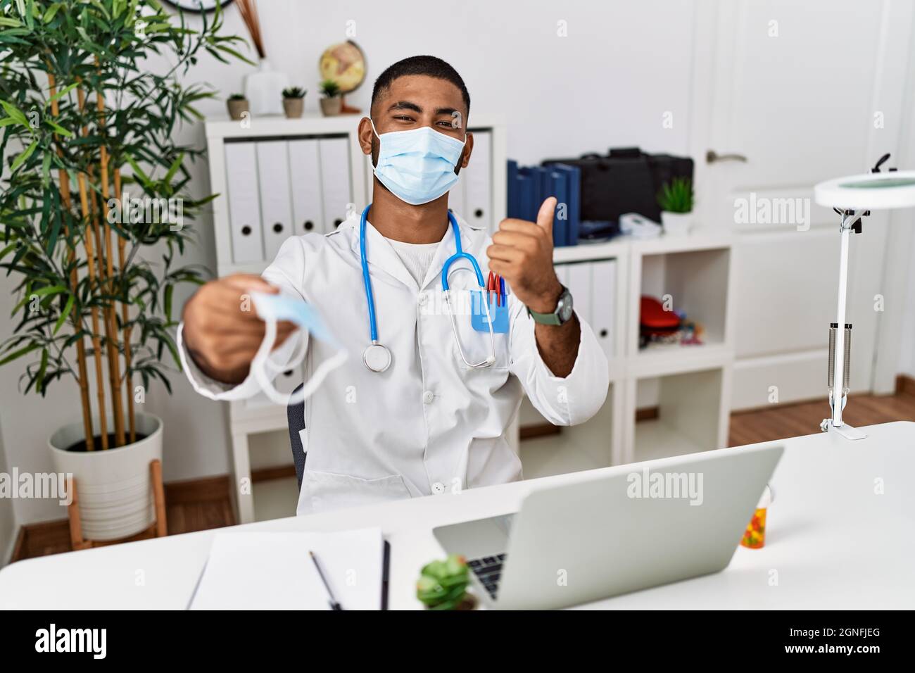 Young indian doctor offering safety mask smiling happy and positive ...