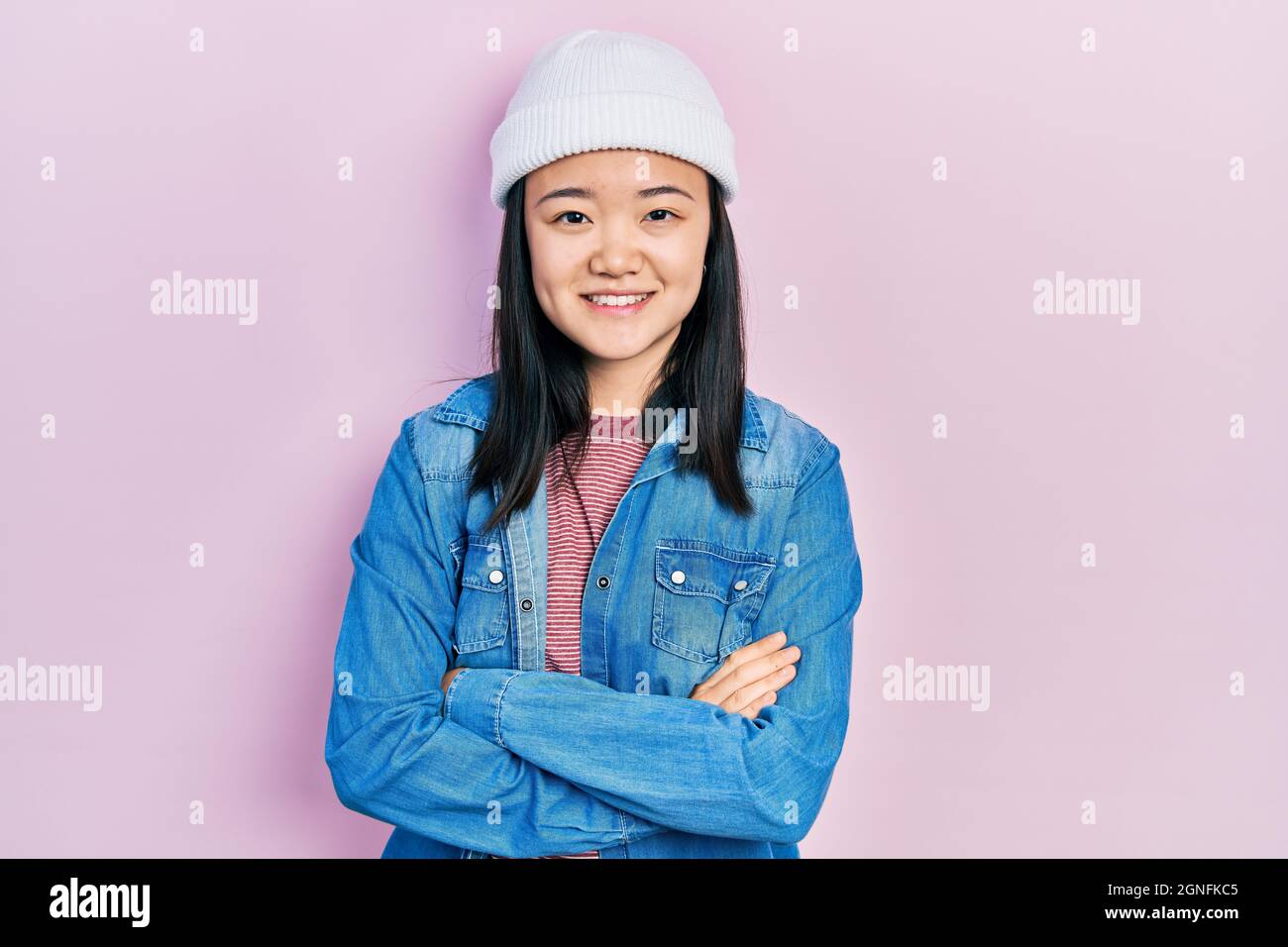 Young chinese girl wearing cute wool cap happy face smiling with crossed arms looking at the camera. positive person. Stock Photo