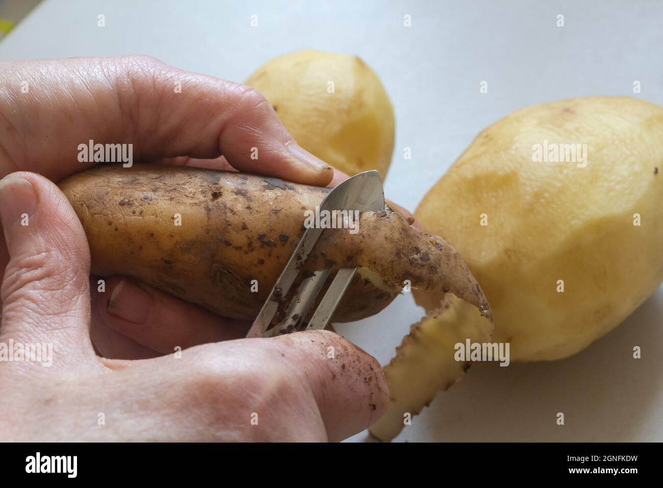To peel a potato with a knife peeler Stock Photo
