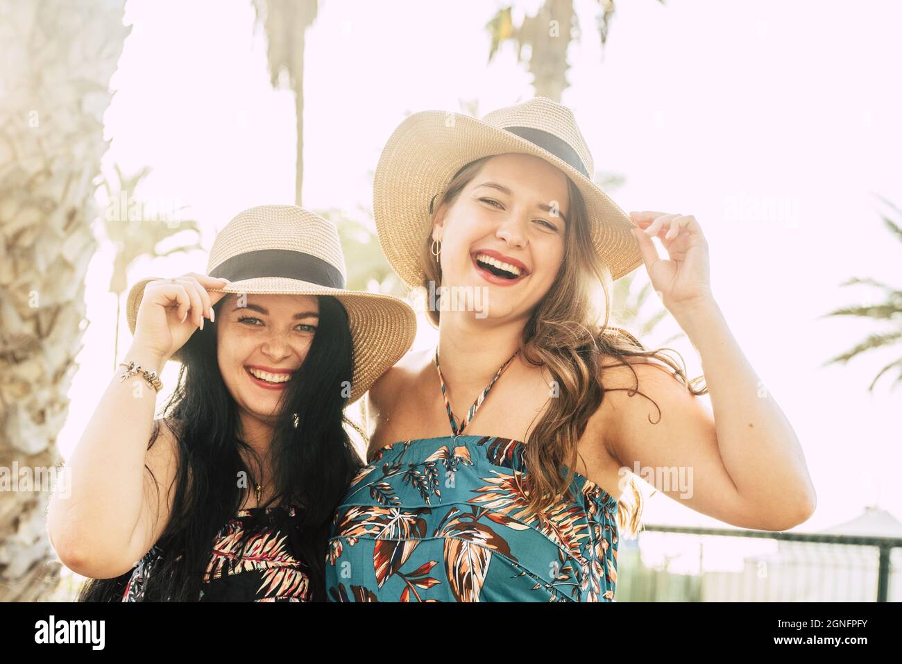 Portrait of two beautiful and cheerful female friends holding straw hats outdoors during summer holiday. Joyful fashionable female tourists with straw Stock Photo