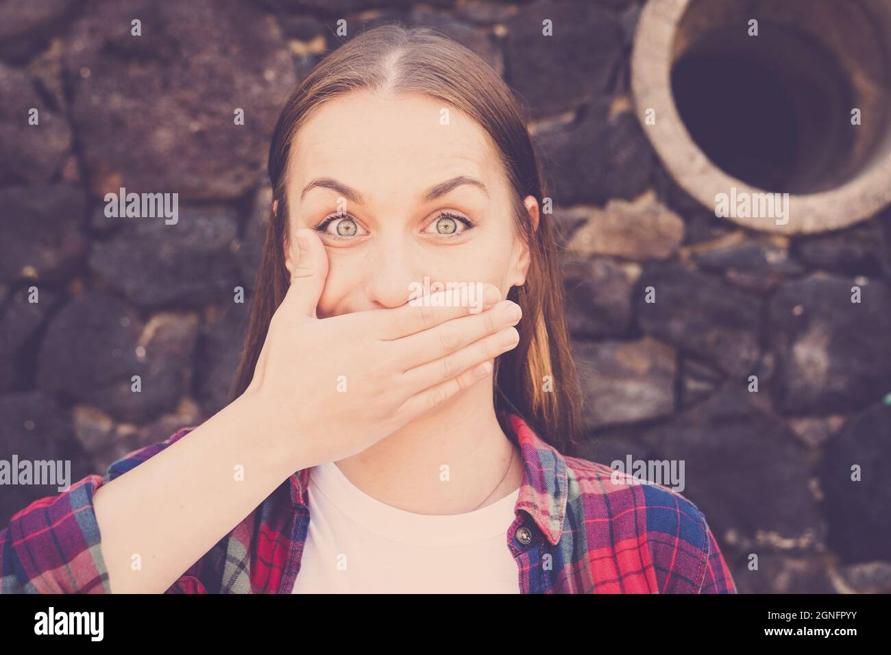 Close up of shocked woman covering mouth with hand standing against stone wall. Portrait of beautiful woman with pierced nose. Woman covering her mout Stock Photo