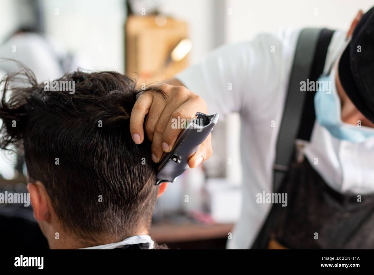 Barber with face mask using hair clipper on client. Stylist cutting hair Stock Photo