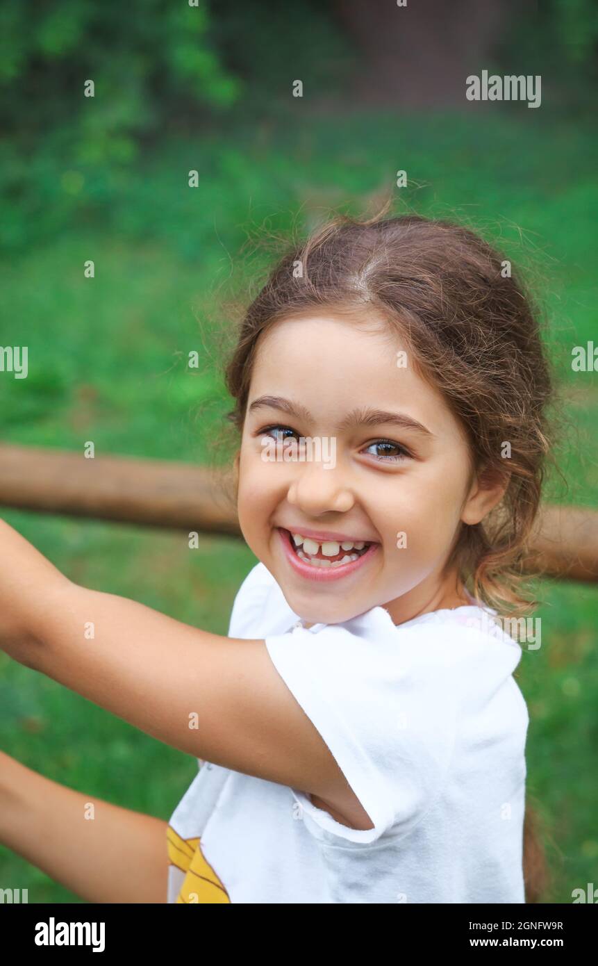 Child playing on outdoor playground. Kids plays on school or kindergarten yard.  Healthy summer activity for children in sunny weather. Cute girl smil Stock Photo