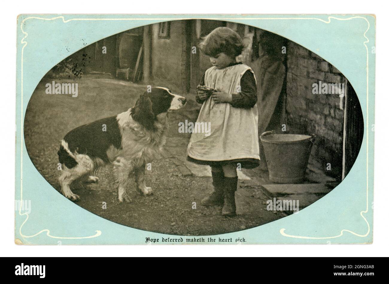 Original sentimental Edwardian greetings real photographic postcard, of a young Edwardian / Victorian girl in a farmyard wearing a pinafore feeding scraps to a waiting springer spaniel  - 'Hope deferred maketh the heart sick' is the inscription. posted April 1904, Published by Marcus Ward & Co. U.K. Stock Photo