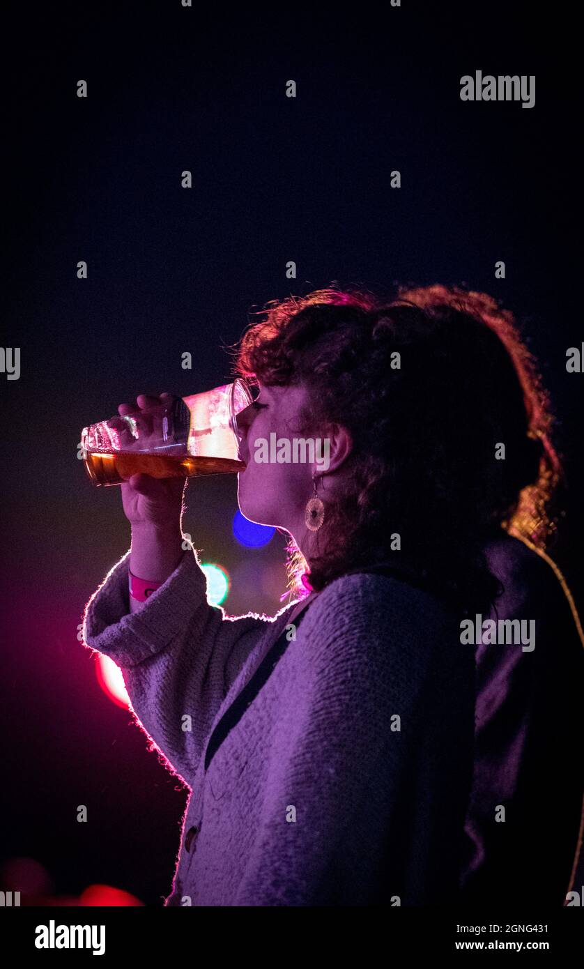 Female drinking a pint of beer from a plastic pint glass silhouetted against coloured lighting. Stock Photo