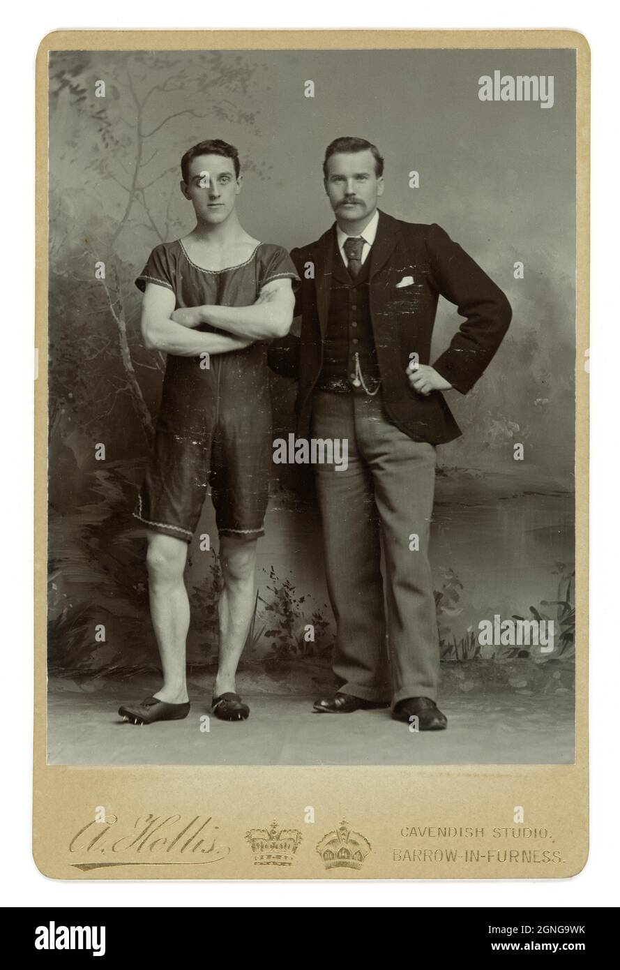Original very sharp and clear image from the Edwardian era. This is a superb cabinet card photograph of an unknown young athlete or sprinter wearing track spikes with his smartly dressed, handsome trainer by Arthur Hollis from his Cavendish Studio, Barrow-in-Furness, North West England, Cumbria, England, U.K. circa 1903 Stock Photo
