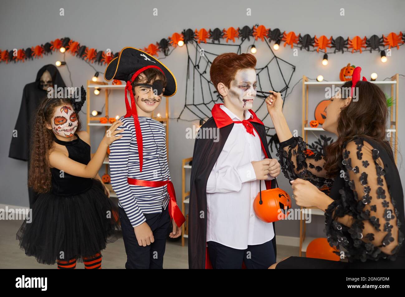 Face paint artist applying spooky makeup to group of kids at fun Halloween party at home Stock Photo