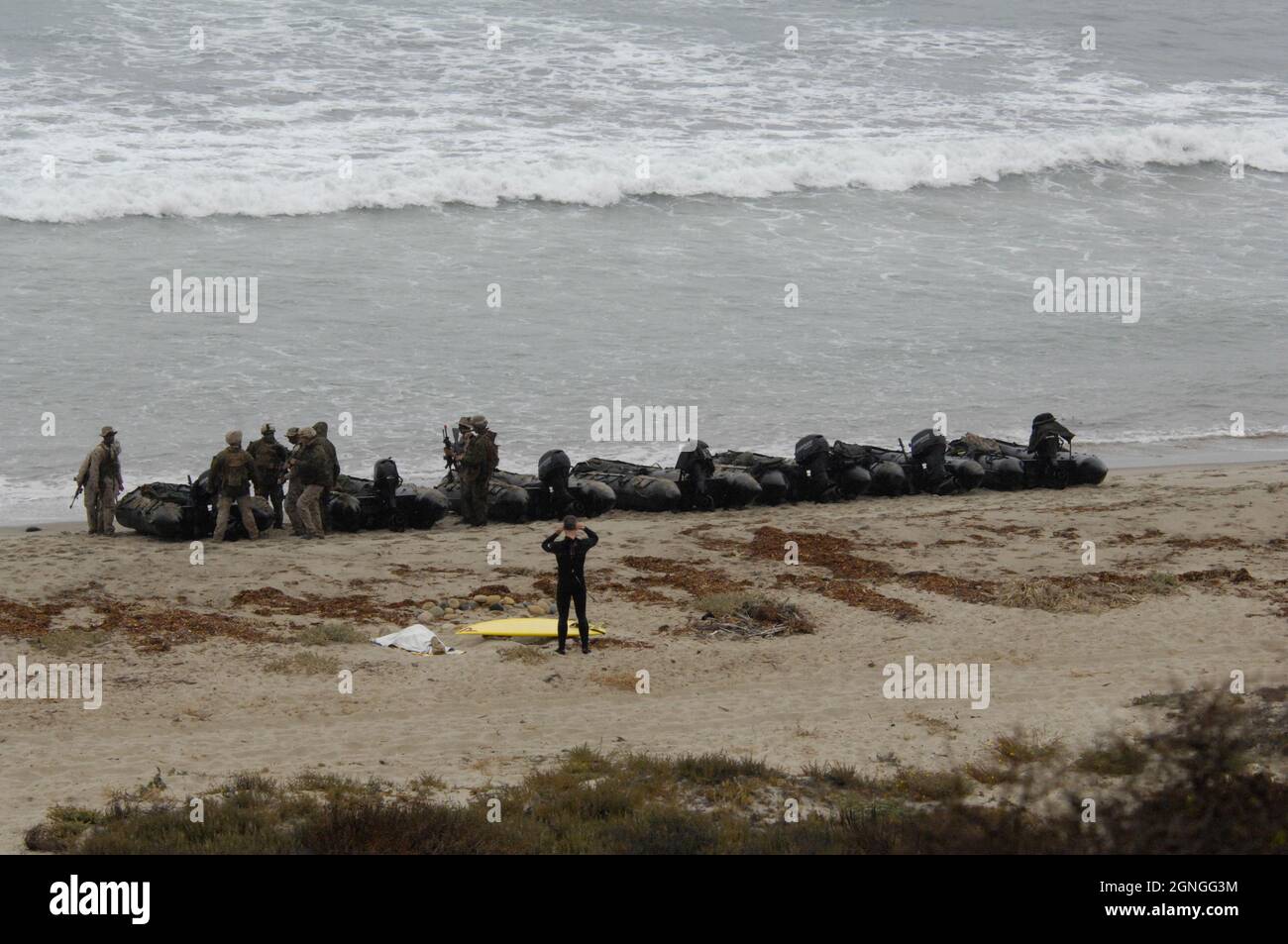 Recon Marines go about their training while watched by a surfer aboard Camp Pendleton, California Stock Photo