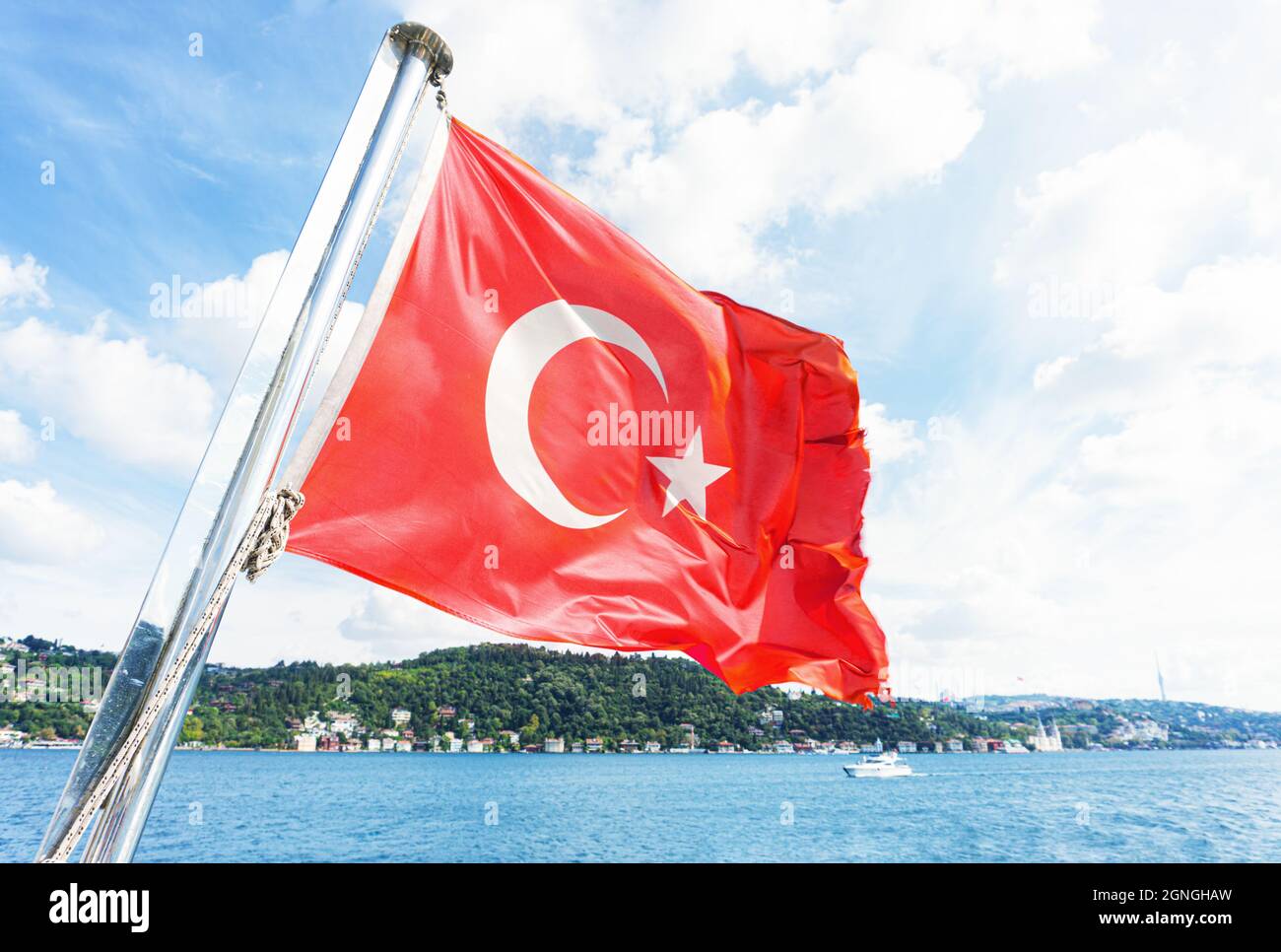 Turkish flag waving against a picturesque coastline of Istanbul. View from the boat during the Bosphorus sightseeing cruise. Stock Photo