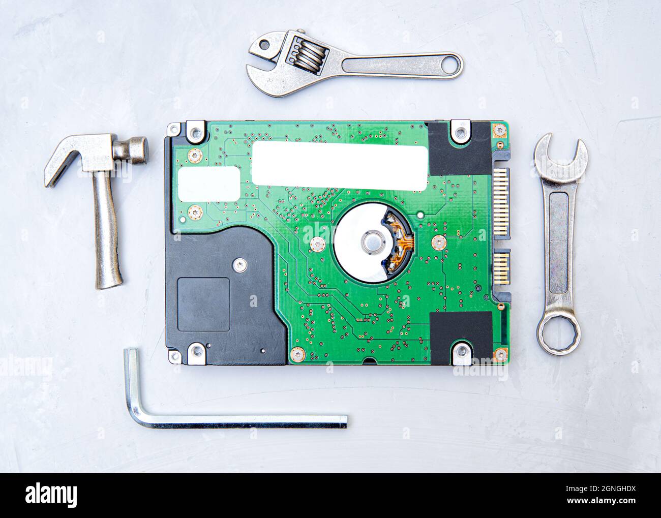 Hard drive disk with no cover framed with small copies of popular hand tools on a concrete background. The concept of using proper tools for the job. Stock Photo