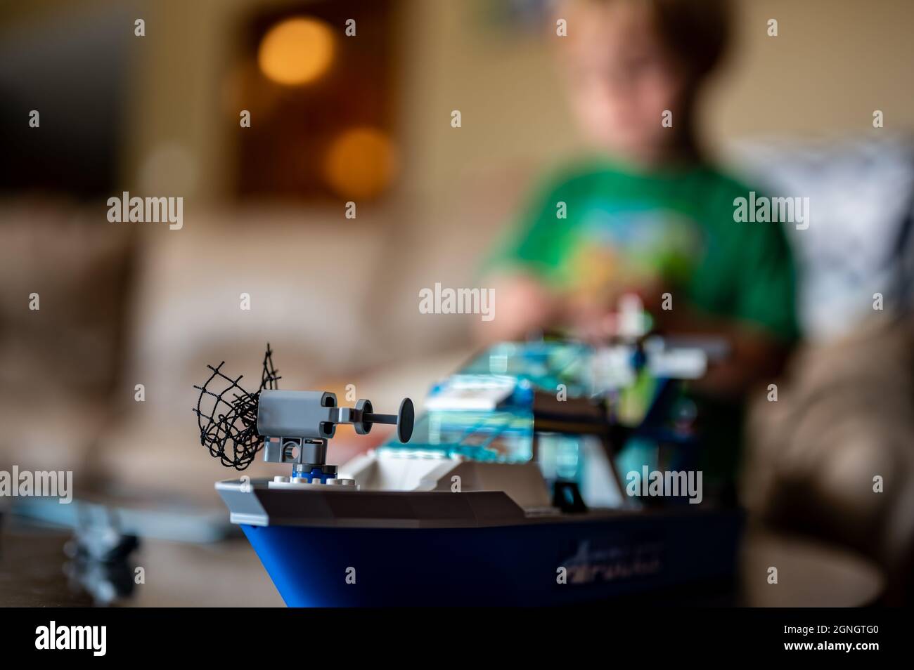 Tiffin, Iowa, USA - 9.2021 - Focus on Lego ship construction set with blurred child in the background playing Stock Photo