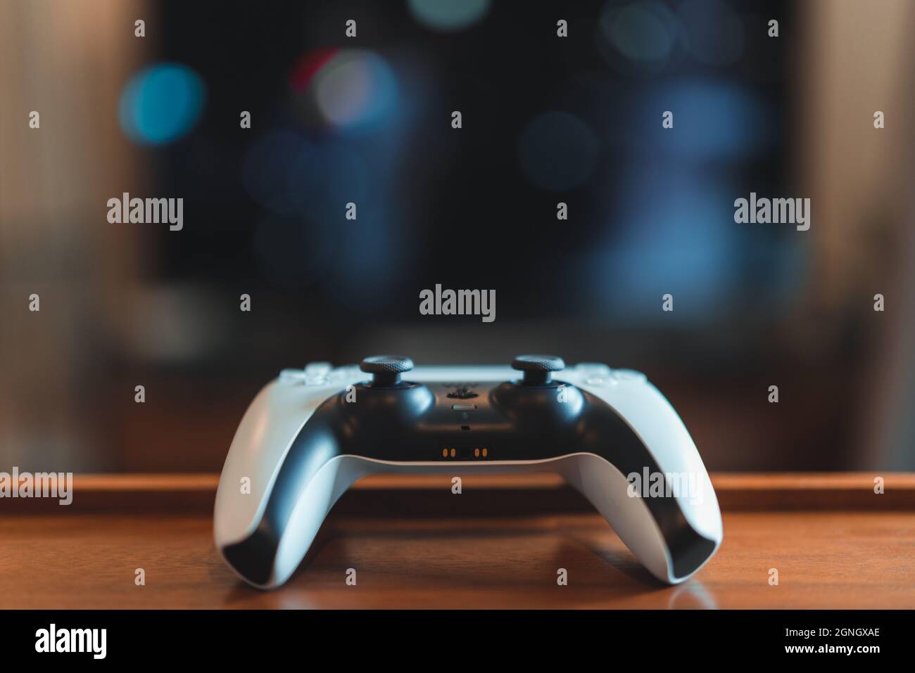London, UK - May 25, 2021: One white Playstation 5 (PS5) controller on the table, tv on background, selective focus. Playstation 5 is the latest video Stock Photo