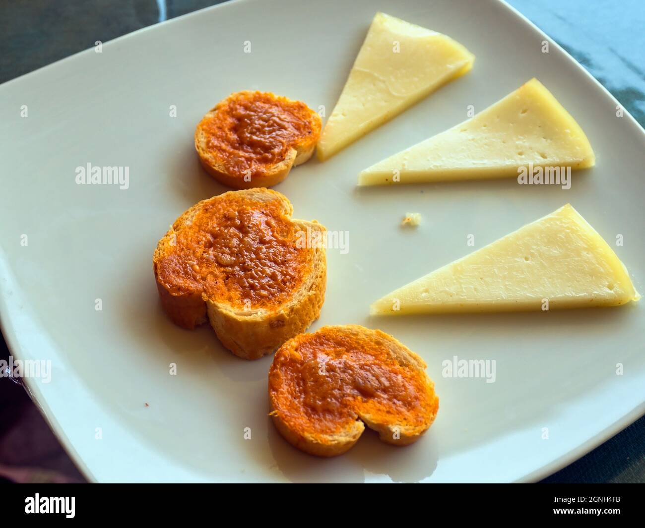 Overhead view of a white plate with three Tapas. Three round small toasts with red Canarian sauce (mojo) and three pieces of cheese. Stock Photo
