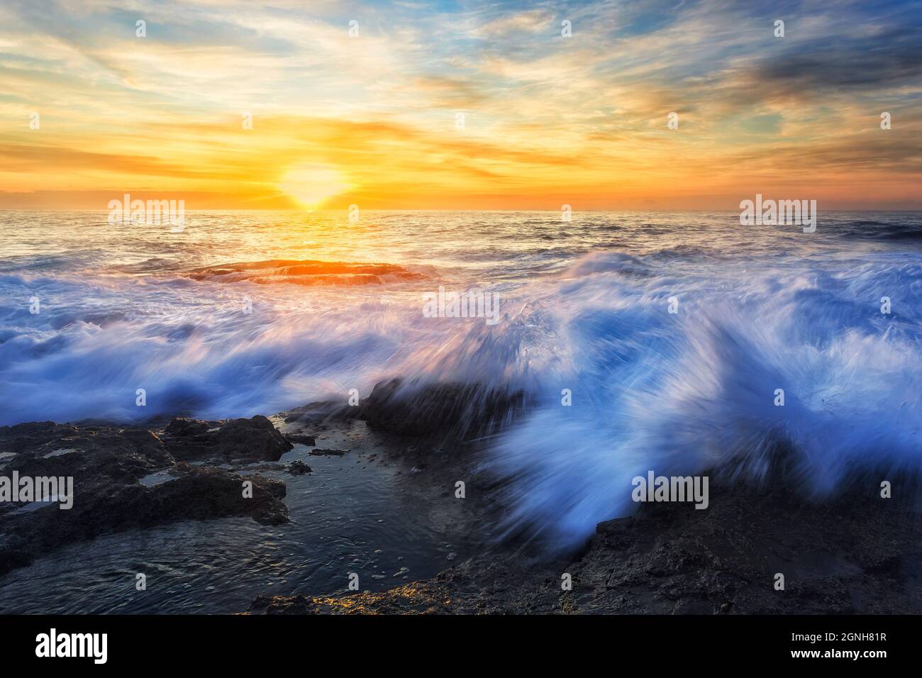 Frozen drops of splashing wave rolling to rocks of TUrimetta beach in Sydney Norther beaches Pacific ocean coast at sunrise. Stock Photo