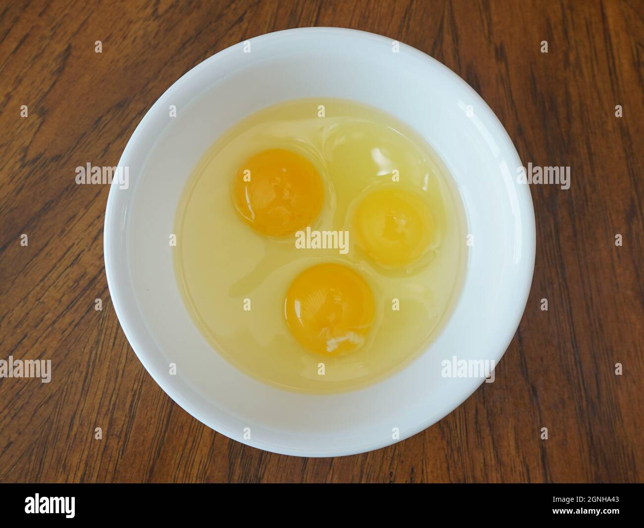 Three eggs in a white bowl on a wood table Stock Photo