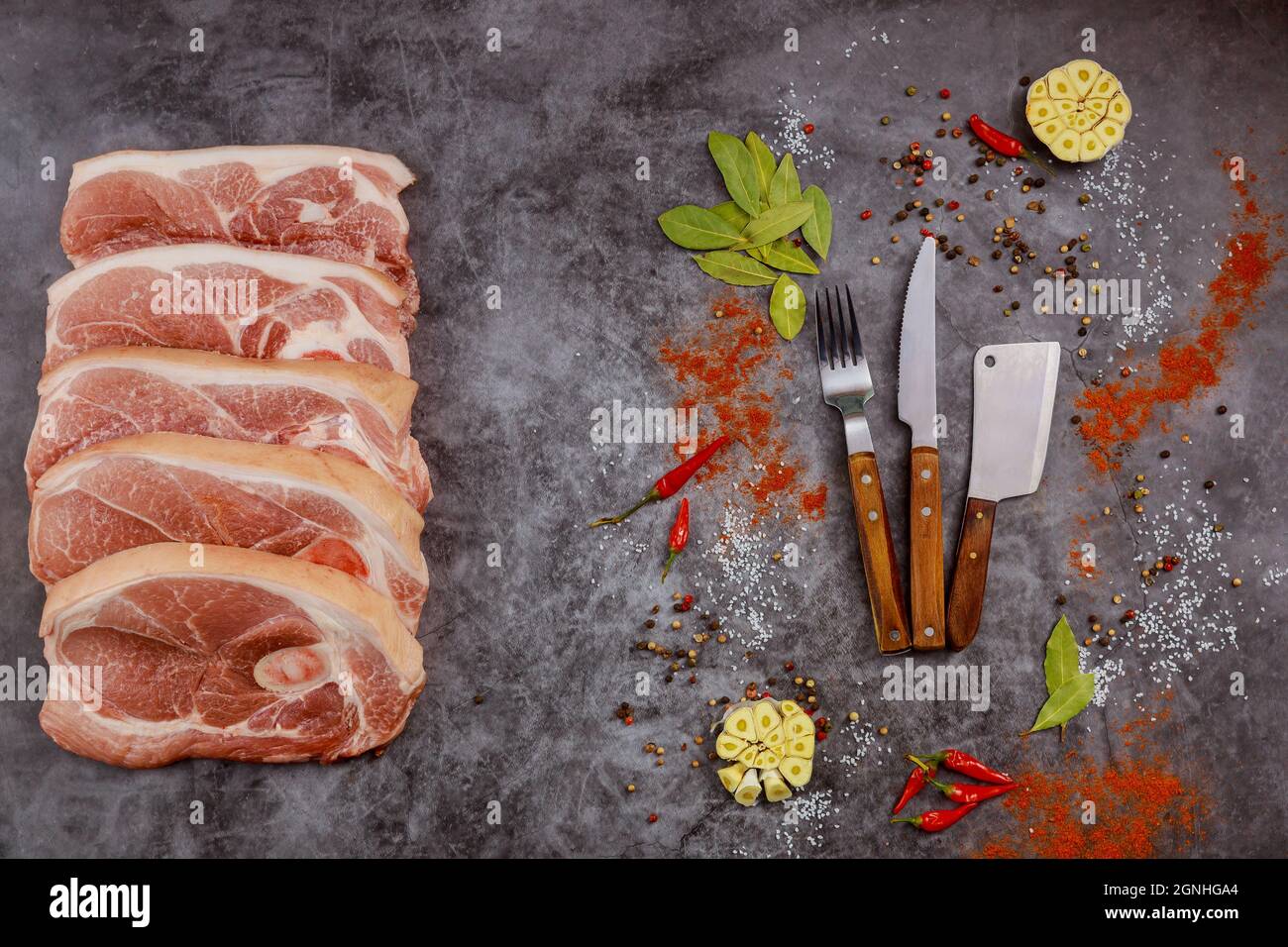 Slices raw pork chops meat with spices and knife on gray background. Top view. Stock Photo