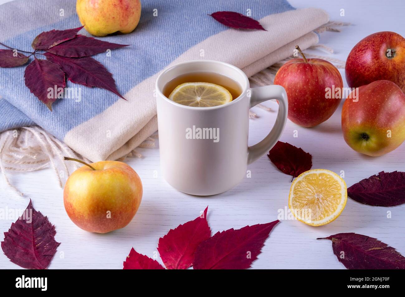 Mug with tea, soft warm scarf, dry autumn leaves and ripe apples Stock Photo