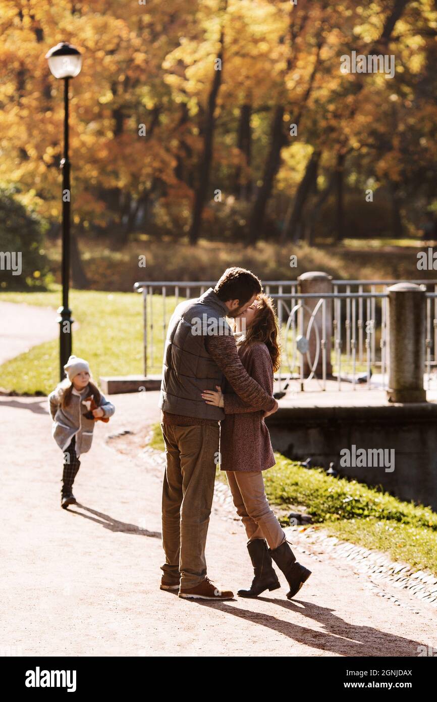 Family love and care: parents couple kiss walking in autumn park together with cute girl daughter Stock Photo