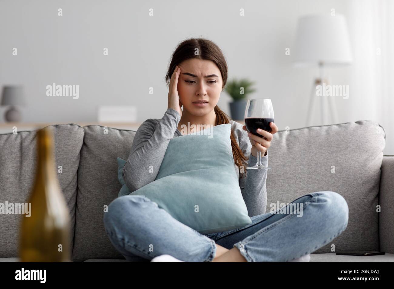 Sad depressed attractive millennial caucasian woman suffering from headache and drinking alcohol at home Stock Photo