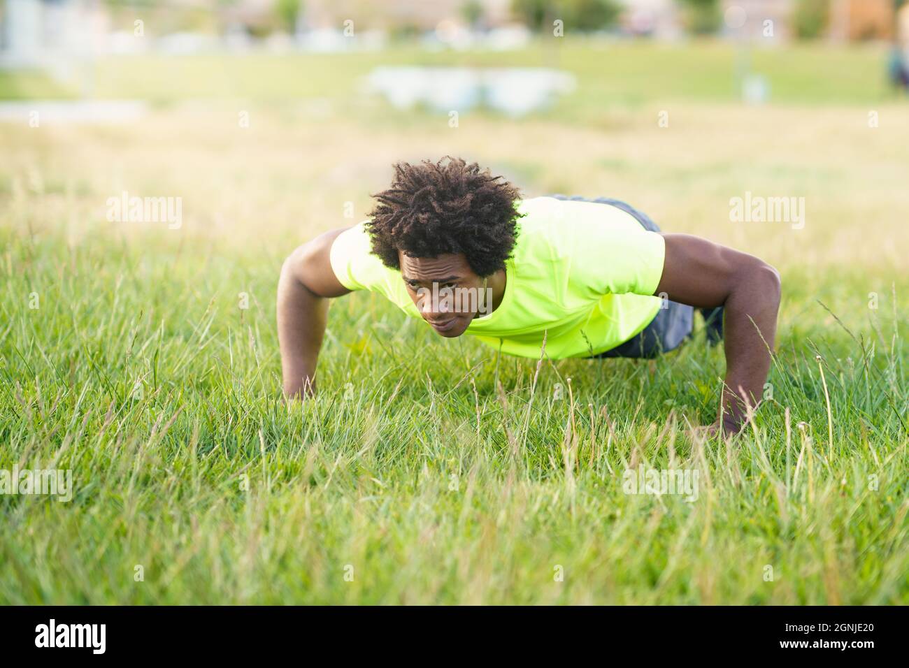 Black man doing push-ups exercising his chest on the grass of an urban ...