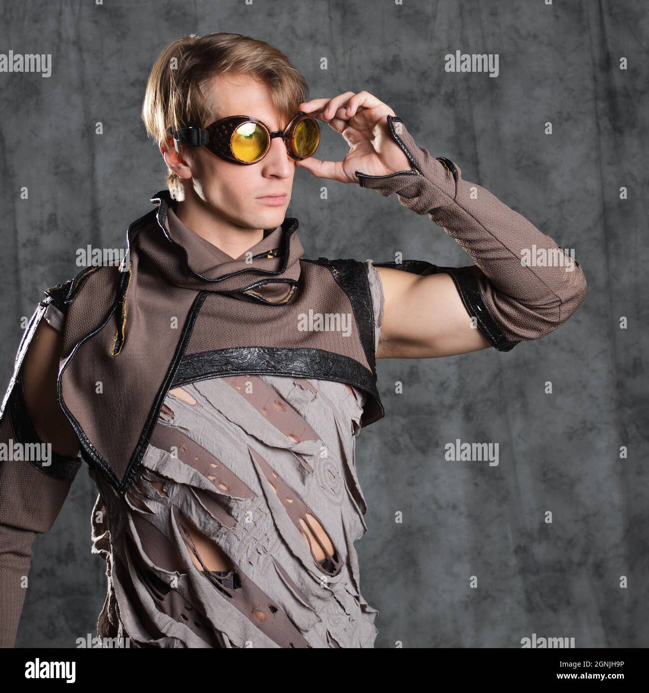 Steampunk or post-apocalyptic style character, a young man in a grunge suit. A jacket with fastened sleeves with slits m goggle flight glasses on his Stock Photo
