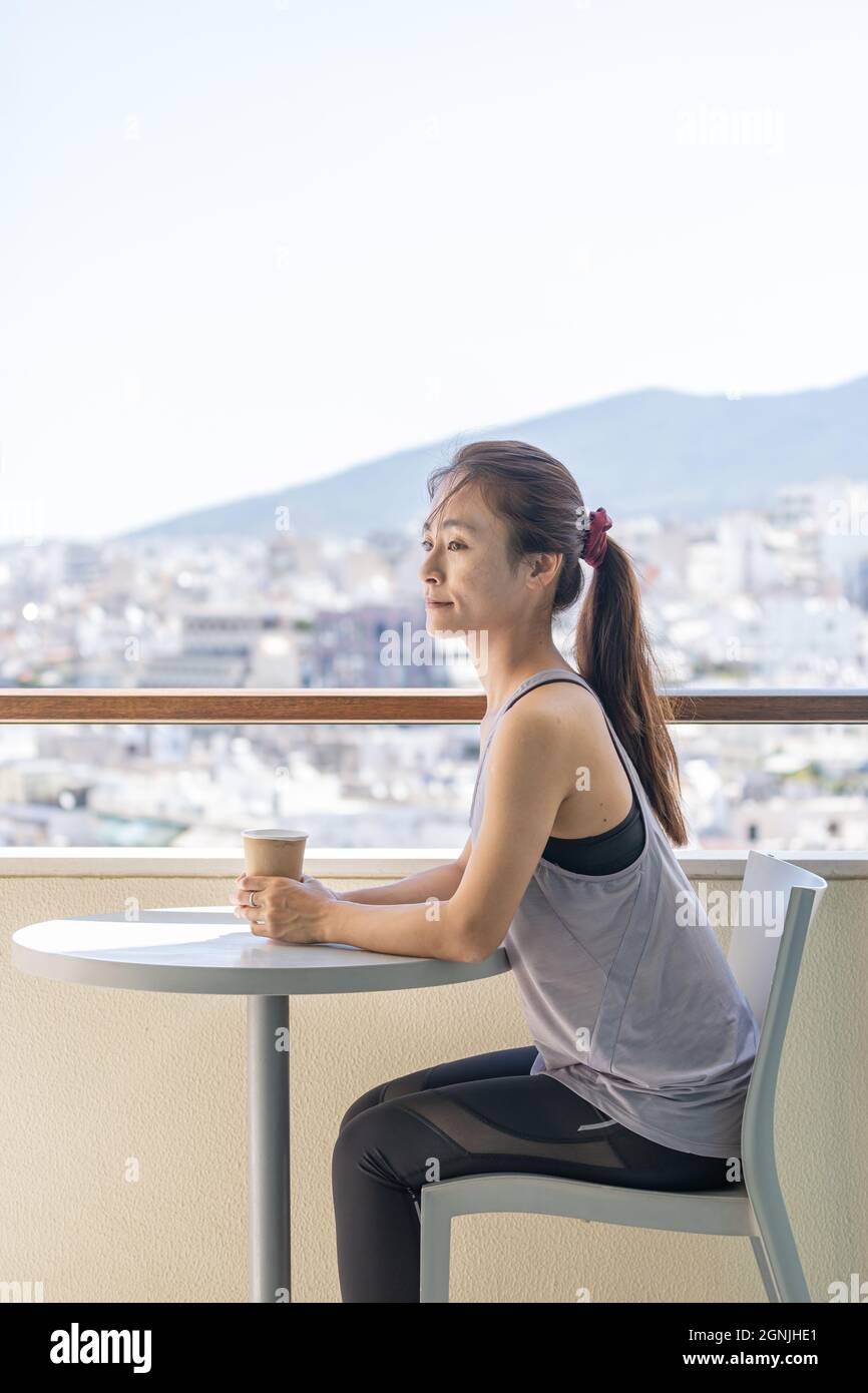 Portrait of an Asian woman with sportswear sitting on the balcony against  city skyline Stock Photo - Alamy