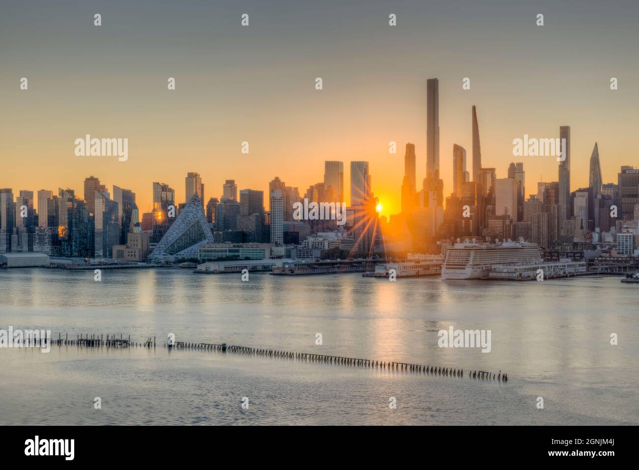 Sunrise in New York City, through buildings in the skyline on the West Side of Manhattan, as viewed over the Hudson River from New Jersey. Stock Photo