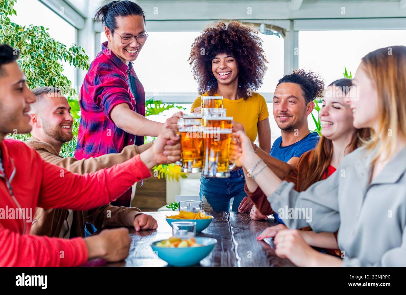 happy group of diverse friends celebrating together on a table in a bar restaurant indoors making celebratoty toast with beers during happy hour Stock Photo
