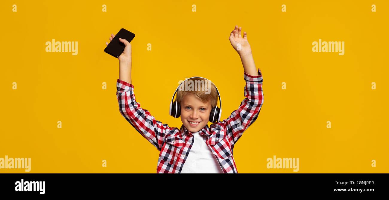 Emotional excited smiling caucasian teen boy in earphones with phone dancing and raising hands Stock Photo