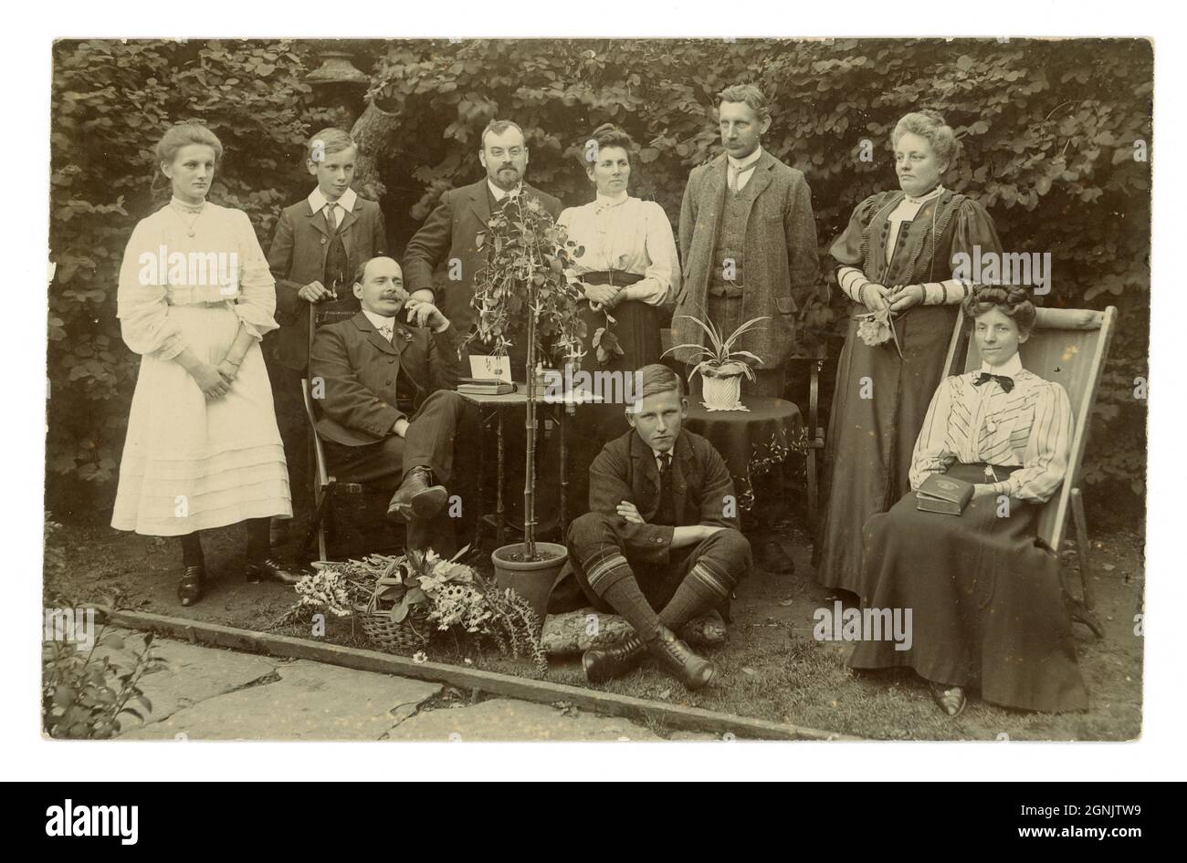 Wonderful original very clear Edwardian real photographic postcard of large Edwardian family group outside in garden on Whit Sunday June 26th 1908, basket of flowers prop, good examples of fashions, men and boy's collars (different styles), women and girl's skirts and blouses, photographer was W.J. Waller, Slinfold, Sussex England, U.K. Stock Photo