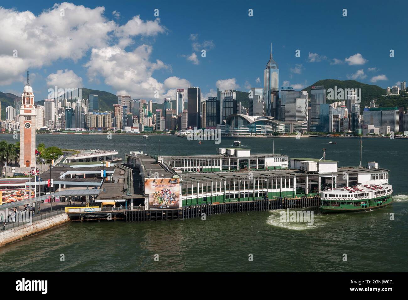 A Star Ferry arrives at Tsim Sha Tsui pier in Kowloon, with Wan Chai and Causeway Bay, Hong Kong Island, visible across Victoria Harbour Stock Photo