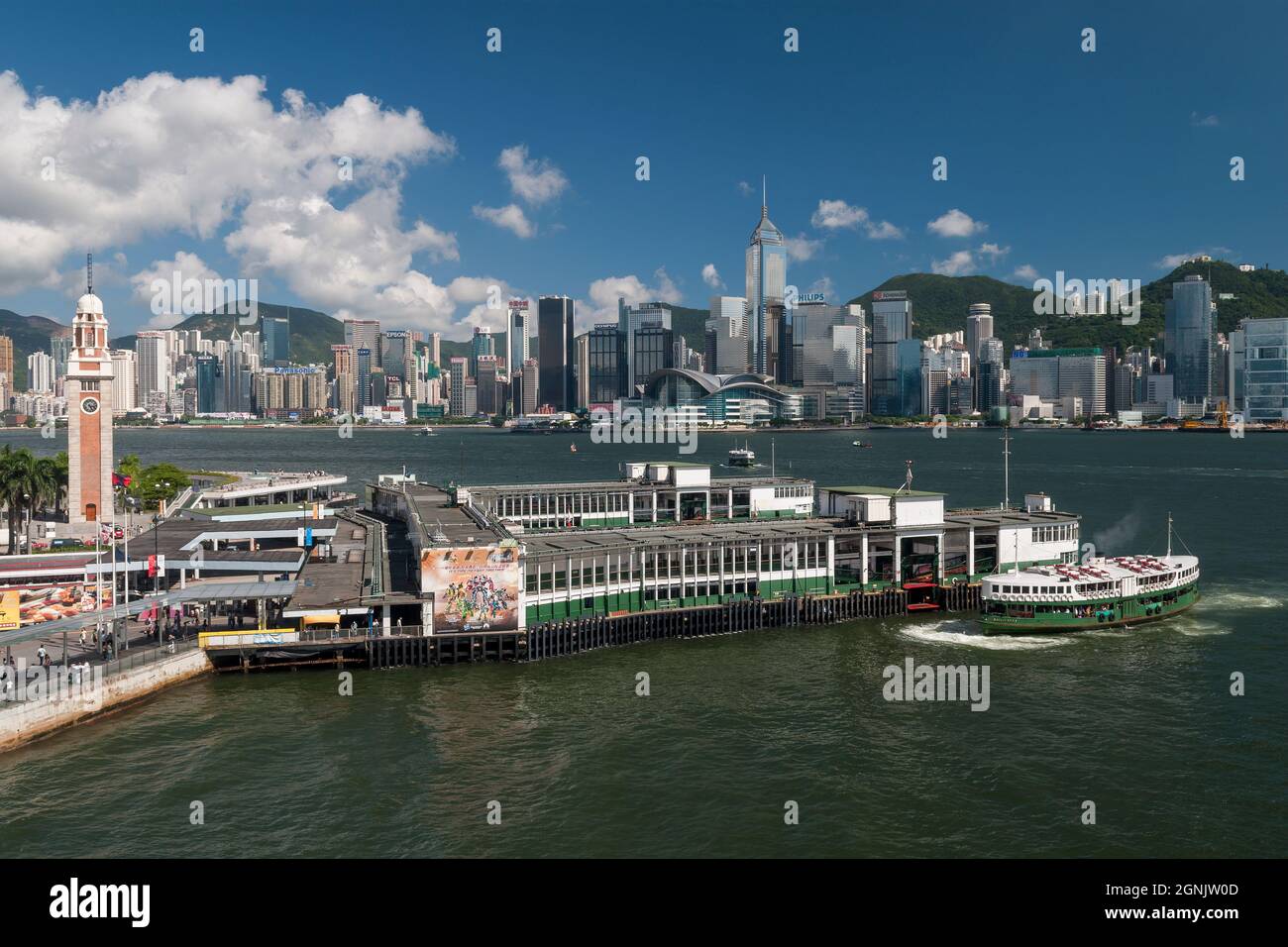 A Star Ferry arrives at Tsim Sha Tsui pier in Kowloon, with Wan Chai and Causeway Bay, Hong Kong Island, visible across Victoria Harbour Stock Photo