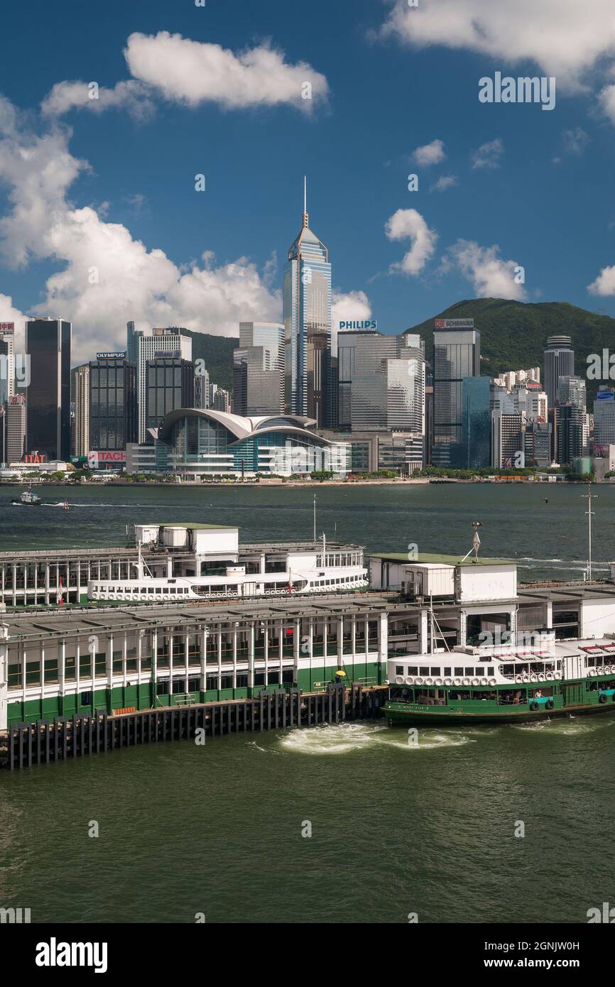 A Star Ferry arrives at Tsim Sha Tsui pier in Kowloon, with Wan Chai, Hong Kong Island, visible across Victoria Harbour Stock Photo