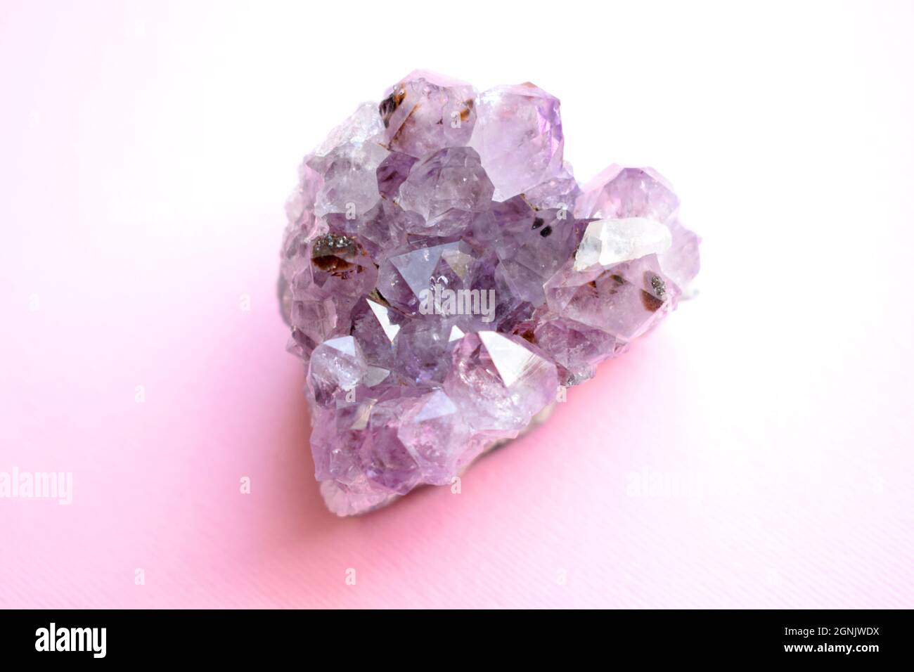 Beautiful druse of natural purple mineral amethyst in the form of a heart on a pink background. Large crystals of a gem. Stock Photo