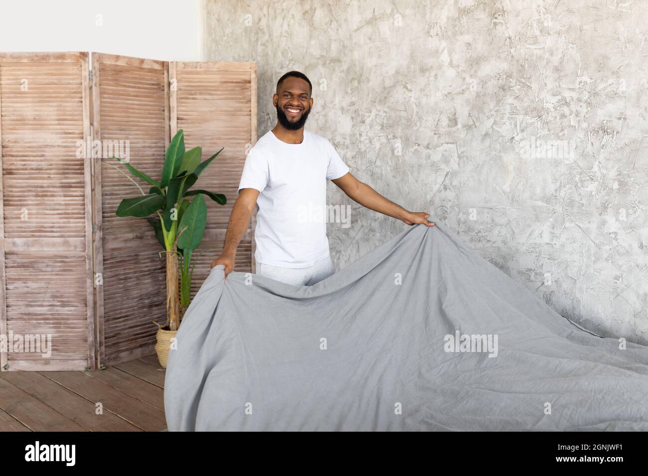 Satisfied young African American man making bed Stock Photo