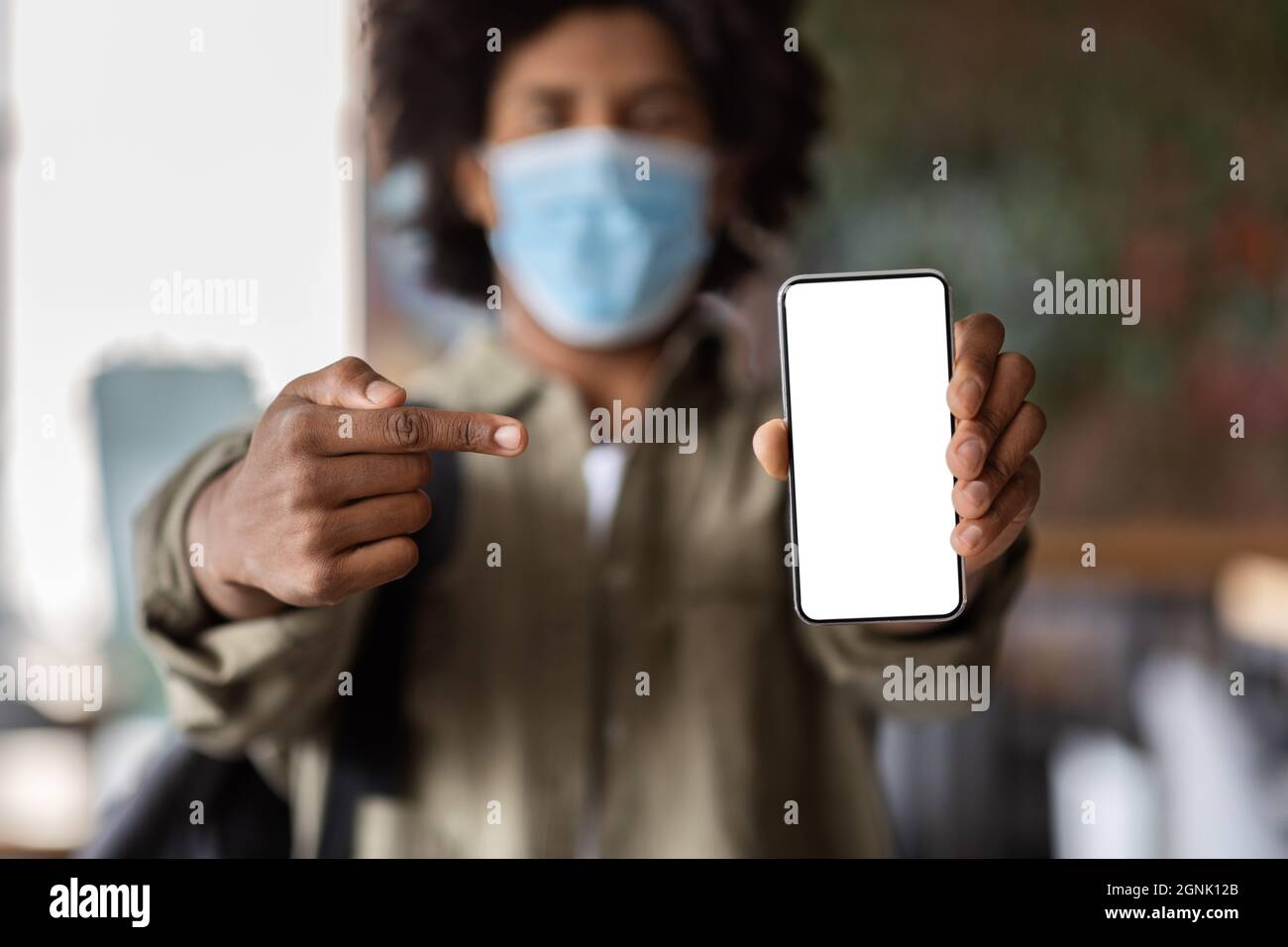 African American Guy In Medical Mask Demonstrating Smartphone With Blank White Screen Stock Photo