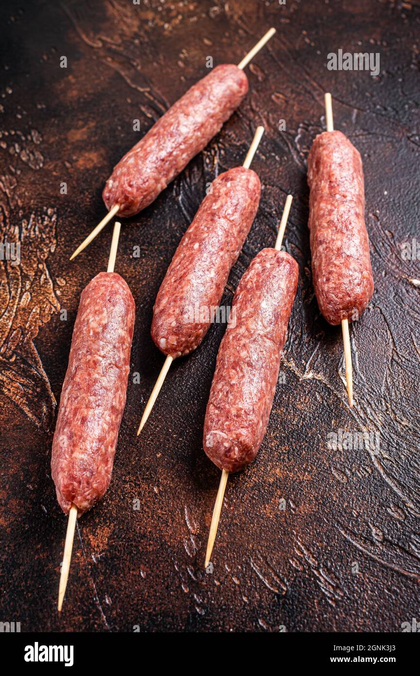 Raw kofta meat kebabs sausages on skewers. Dark background. Top view