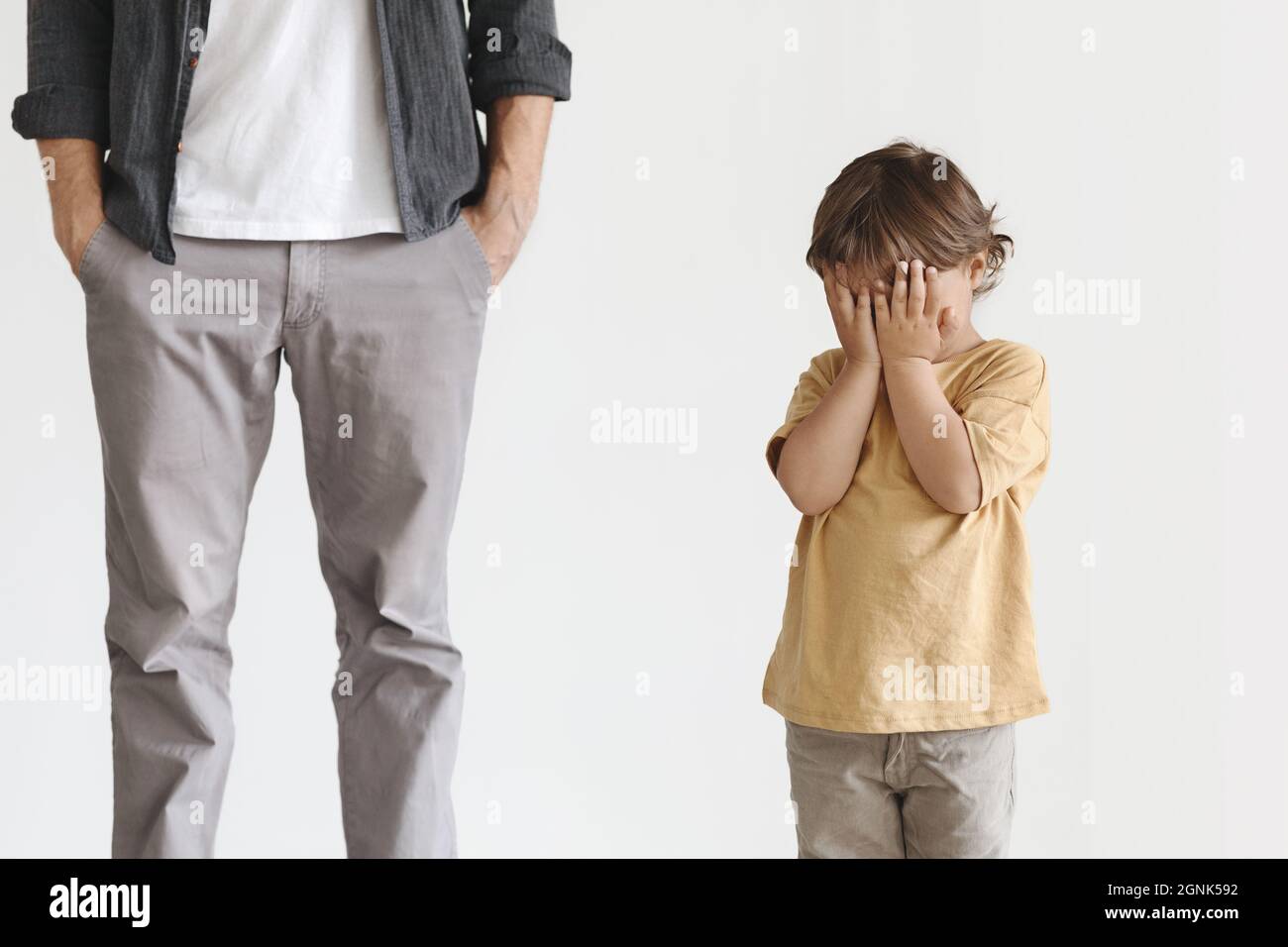 Little baby boy crying, feeling abandoned and lonely, unrecognizable father standing behind with hand in pockets Stock Photo