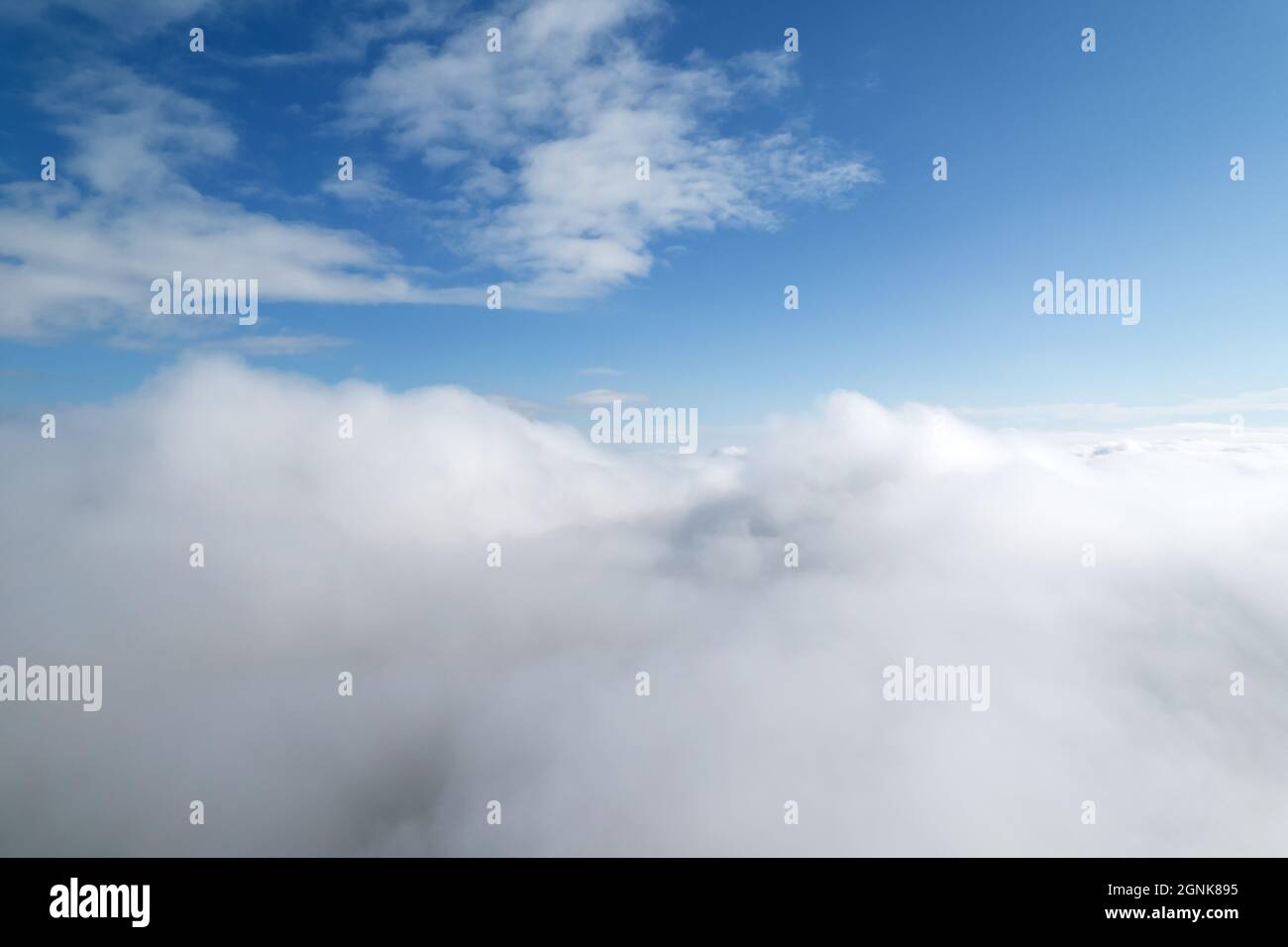 Higher than clouds. Aerial shot of white fluffy clouds and some blue sky in distance while flying above clouds. Beautiful cumulus clouds captured by a Stock Photo