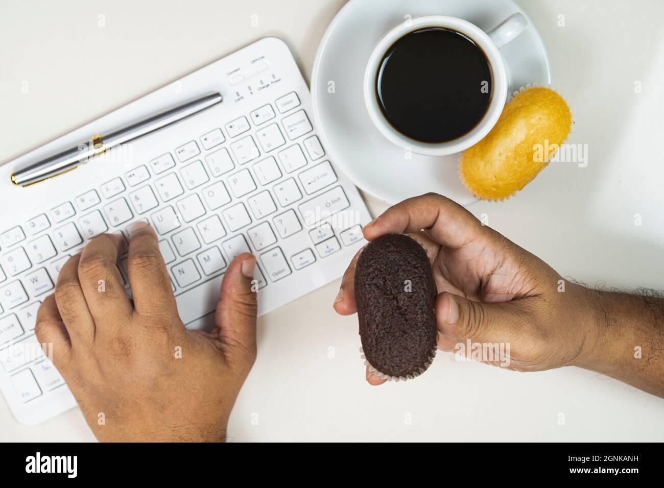Working from home concept. Typing on a keyboard and eating muffins with a cup of coffee. Selective focus points Stock Photo