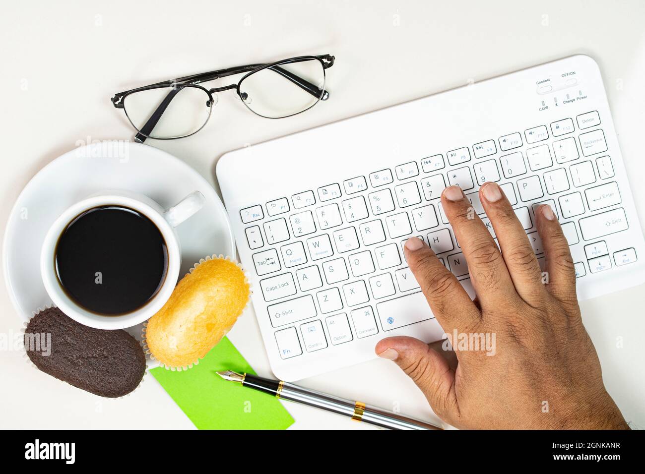 Working from home concept. Hand typing, muffins, pen, notes, spectacles with a cup of coffee. Selective focus points Stock Photo